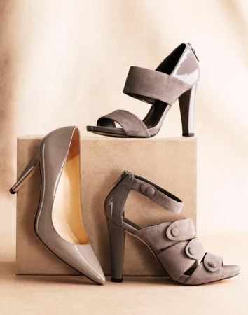Three grey high heel shoes styled on a neutral block against a textured beige backdrop by fashion stylist Kate Mccann.