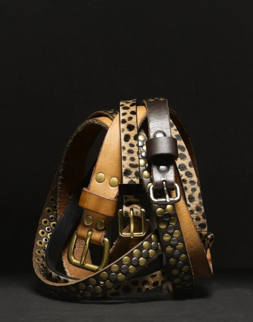 Group of assorted leather belts with buckles, including studded and animal print designs, stacked against a dark background.