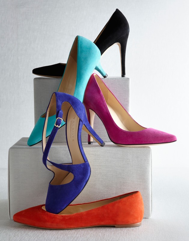 Still life of fashionable women's shoes in black, turquoise, pink, blue, and orange displayed on a stack of gray, upholstered blocks.