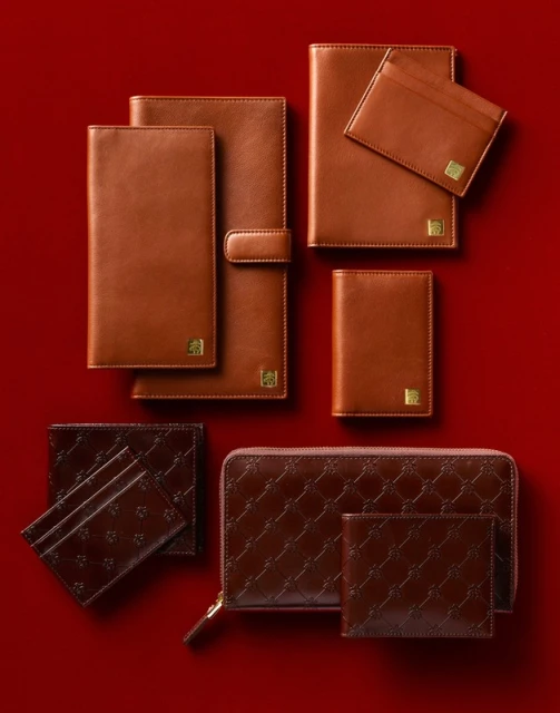 Elevated shot of tan and dark brown leather wallets, cardholders, notebook covers, and zippered pouch, arranged on a red background.