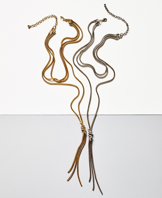 Two multi-strand metal lariat necklaces, one gold and one silver, displayed against a split white and grey seamless background.
