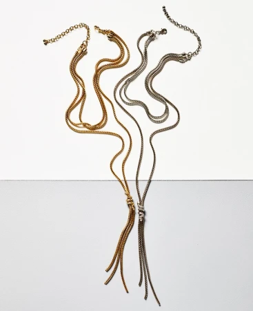 Two multi-strand metal lariat necklaces, one gold and one silver, displayed against a split white and grey seamless background.
