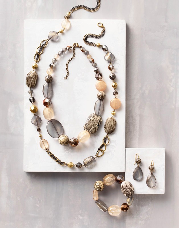 Elegant jewelry set featuring a necklace, bracelet, and earrings, showcasing neutral tones and faceted beads on a white surface. 