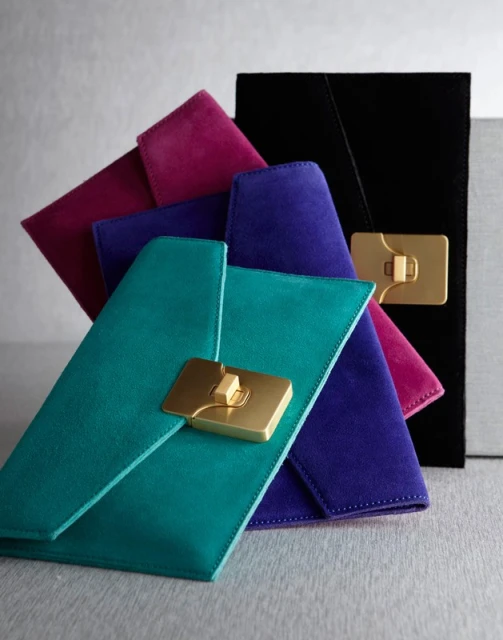 Stacked arrangement of colorful clutch bags, featuring various shades of pink, purple, turquoise, and black, accessorized with gold clasps.