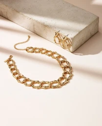 Gold chain necklace and matching hoop earrings displayed on a concrete block with natural directional lighting.