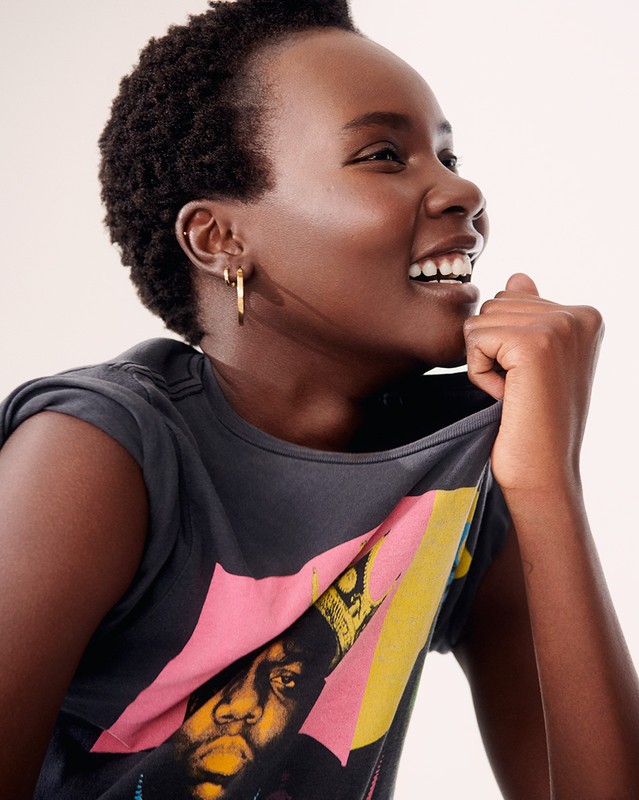 Woman smiles and wears a graphic tee shirt with image of The Notorious B.I.G. in a bright, neutral studio setting.