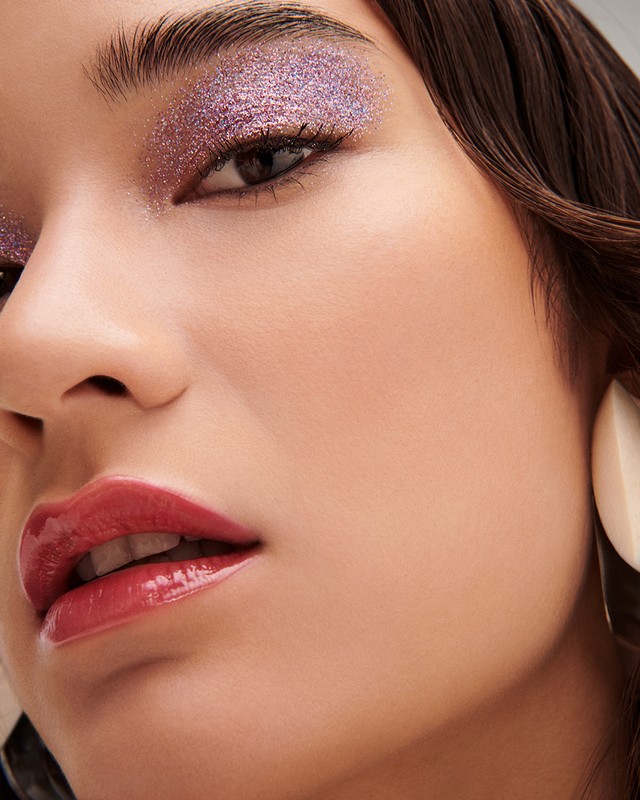 Close-up beauty portrait of a woman with shimmering purple eyeshadow and glossy red lips photographed by Kate Powers.