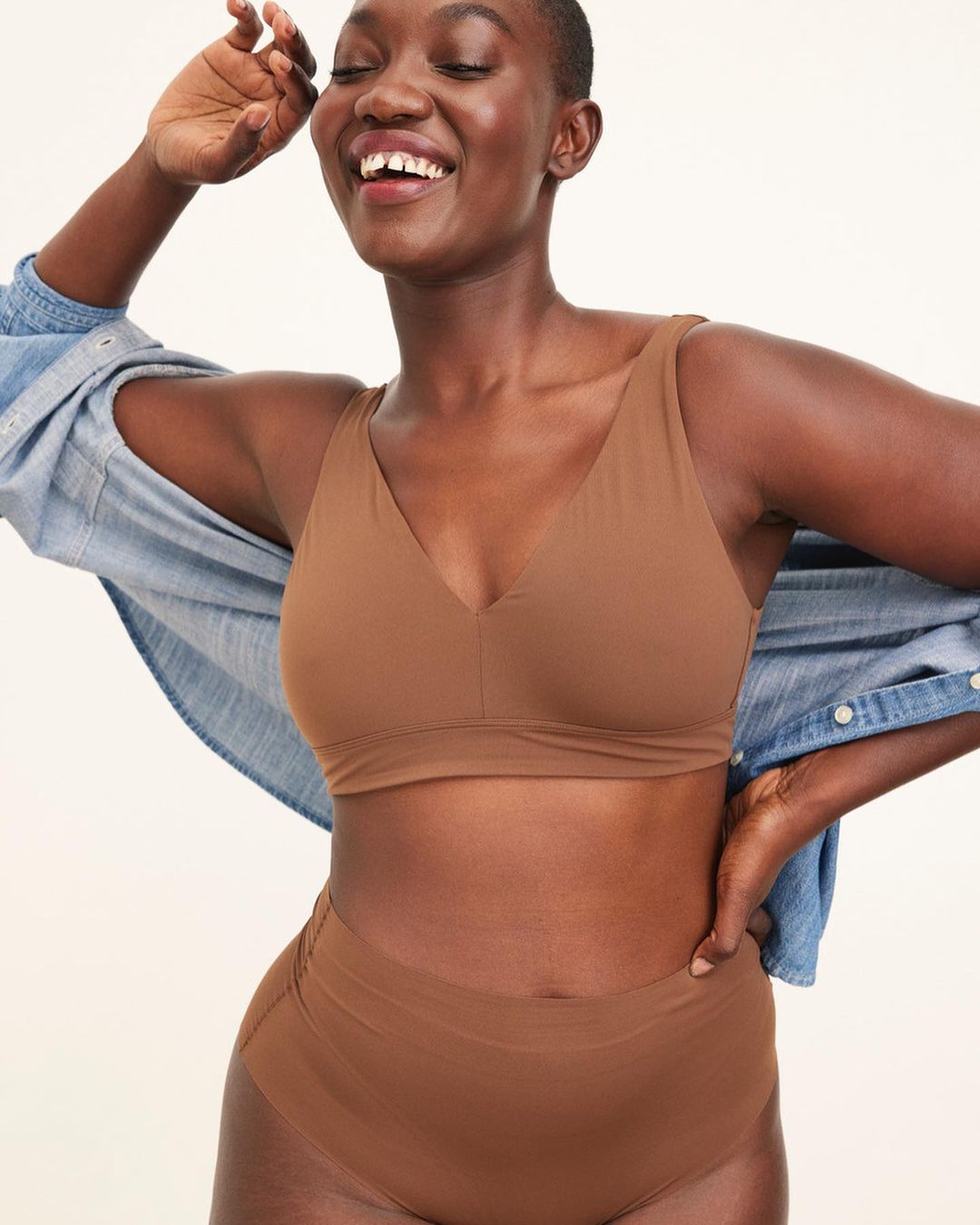 Black woman smiling wearing a brown bra and high-waisted briefs with an open denim shirt
