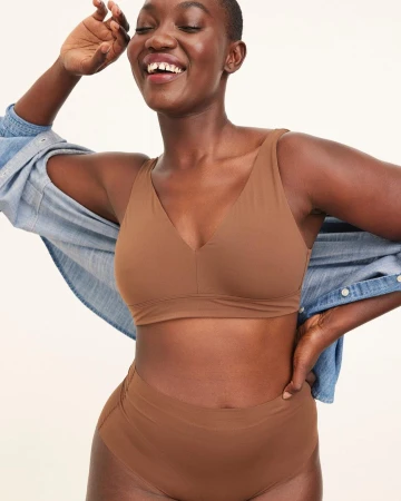 Black woman smiling wearing a brown bra and high-waisted briefs with an open denim shirt