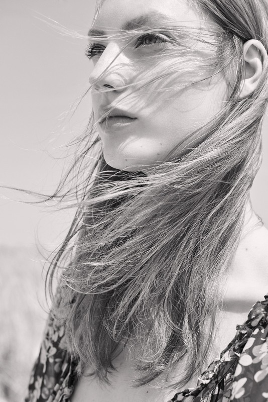 Close-up portrait of a woman with long hair blowing in the wind wearing a floral patterned garment