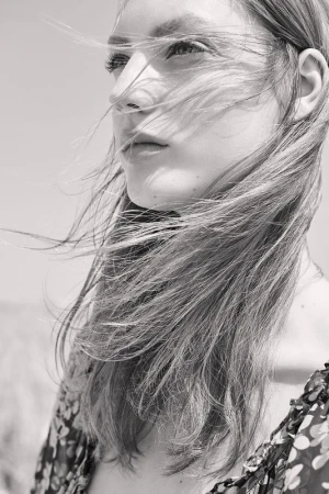 Close-up portrait of a woman with long hair blowing in the wind wearing a floral patterned garment