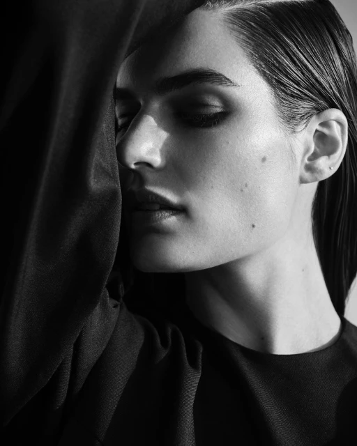 Black and white portrait of a woman with closed eyes and smooth hair, a portion of her face covered by a dark fabric.