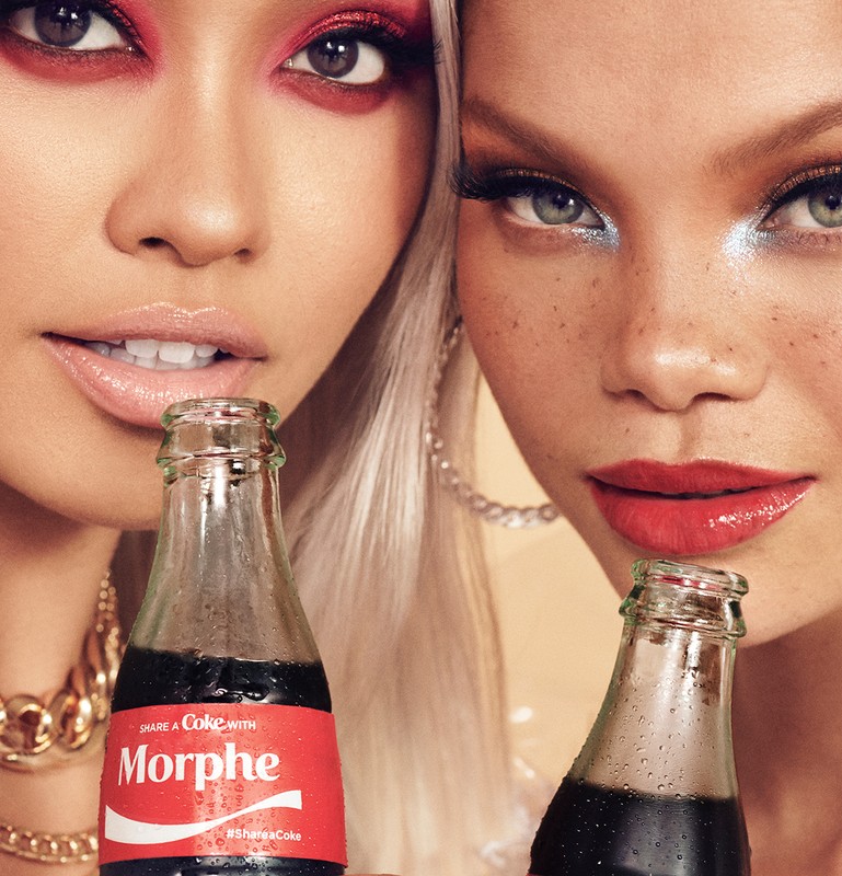 Two fashion models pose with branded Coca-Cola bottles showcasing Morphe makeup, adorned with red and blue eye makeup and gold jewelry.