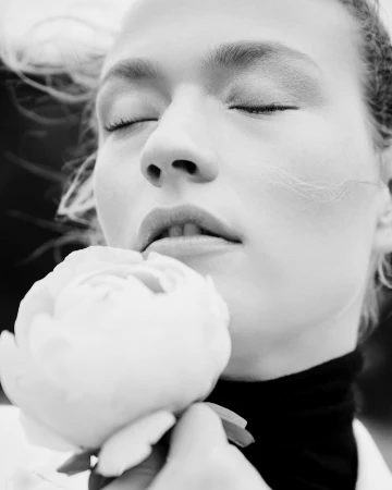 Close-up monochrome portrait of a woman with closed eyes holding a white flower near her face by Kate Powers.
