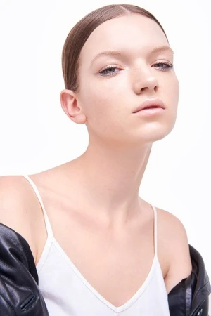 Close-up studio shot of a young adult female model in a white tank top and black jacket, gazing directly at the camera on a white background.