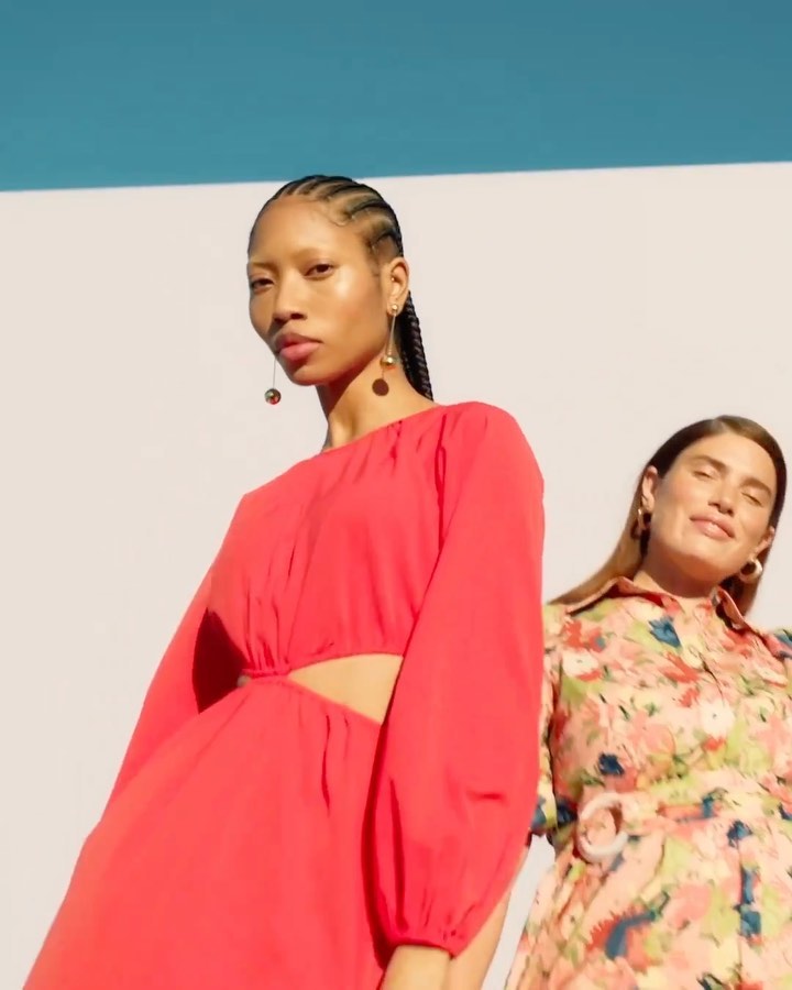 Two women model colorful dresses in an outdoor setting, featuring one in a bright pink dress and the other in a floral print dress.