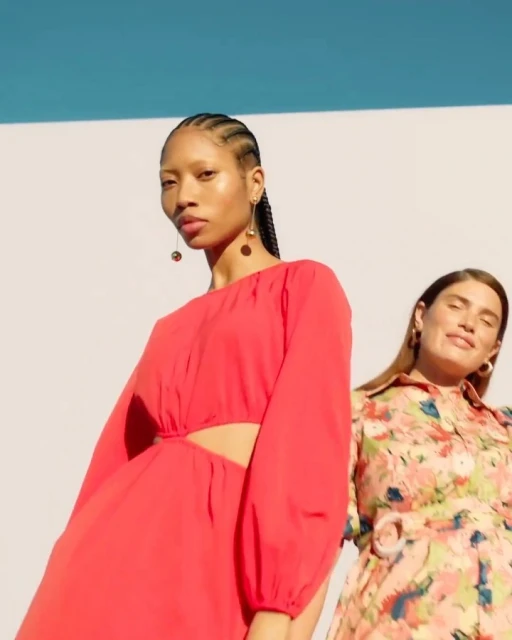 Two women model colorful dresses in an outdoor setting, featuring one in a bright pink dress and the other in a floral print dress.