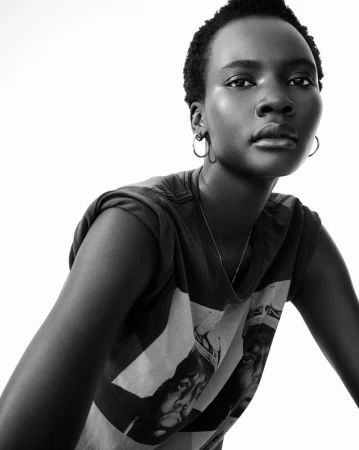 Black woman with short hair wearing a graphic t-shirt and hoop earrings against a white background