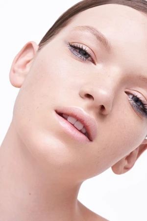 Close up beauty portrait of a young woman with soft makeup and light freckles against a seamless white background.