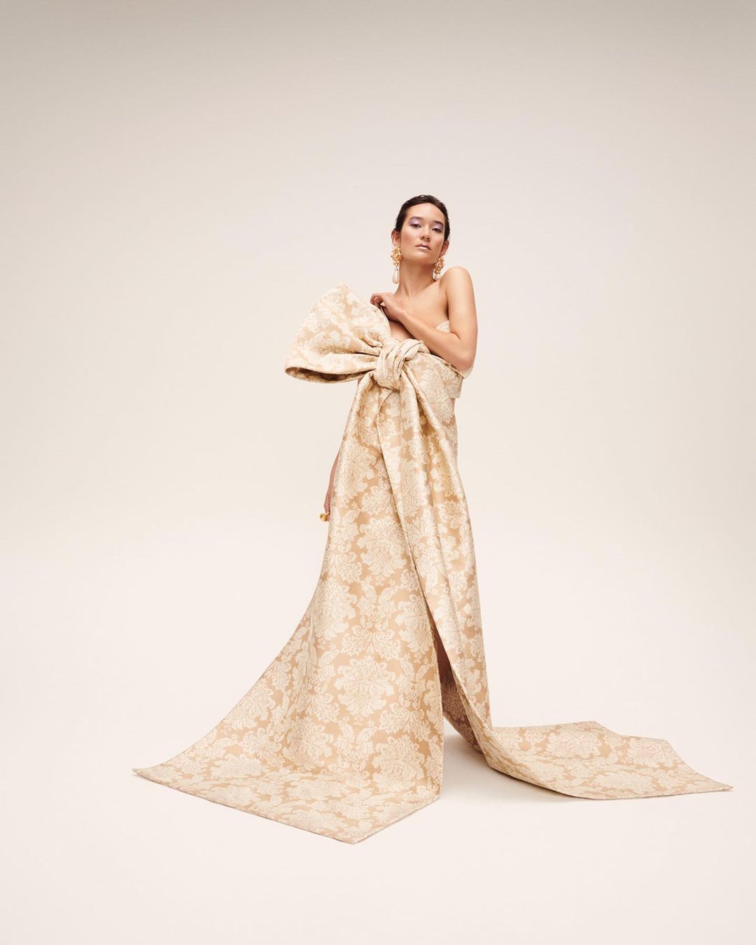 Model wearing a large patterned bow gown standing against a plain white background