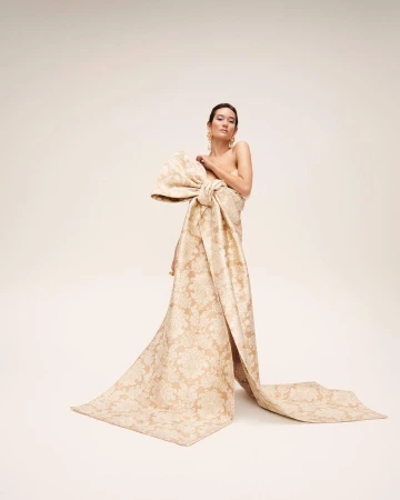 Model wearing a large patterned bow gown standing against a plain white background