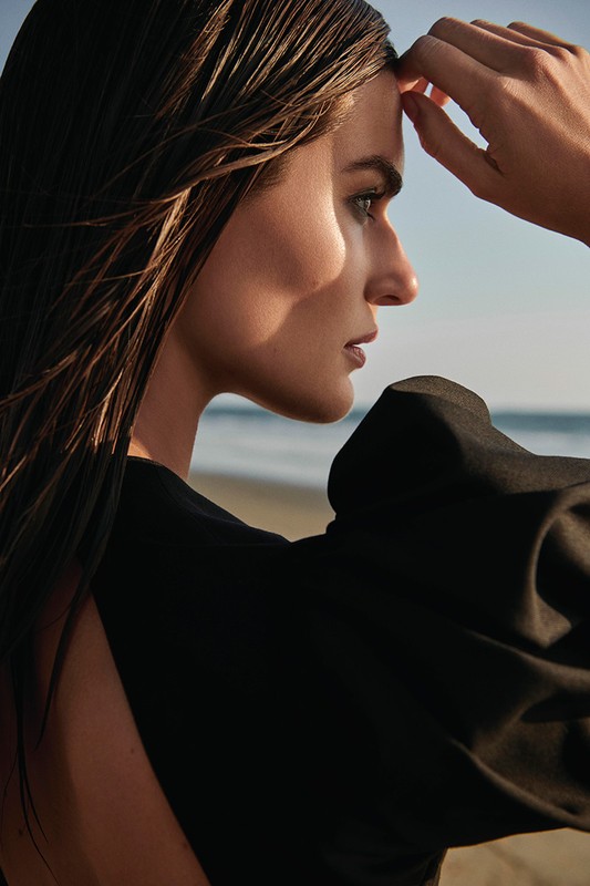 Profile portrait of a woman with wet hair wearing a black top outdoors by the beach, photographed by Kate Powers.
