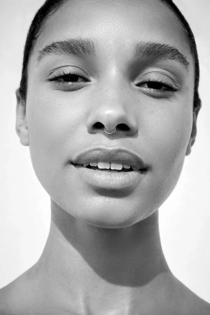 Striking black and white portrait of a young adult female with a nose ring, showcasing minimalist beauty and neutral tones in a close-up shot.