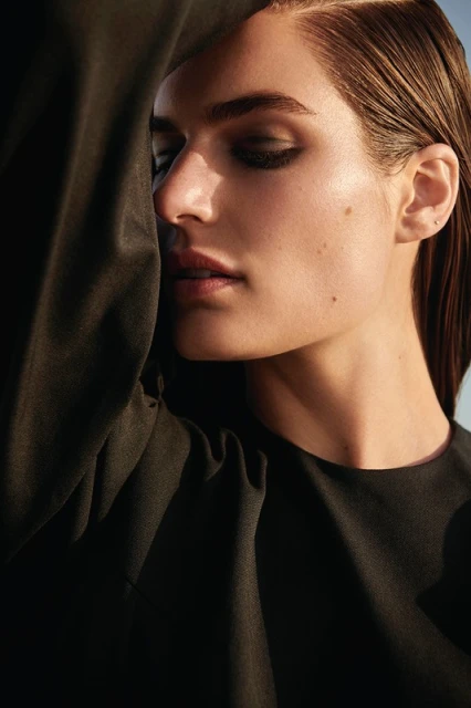 Close-up portrait of a woman with sleek brunette hair, wearing a black top. The lighting highlights her face and the texture of her clothing.