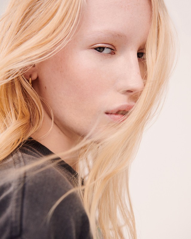 Close-up portrait of a blonde woman wearing a dark t-shirt against a plain white background, photographed by Kate Powers.