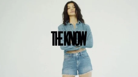 Model in denim shirt and denim shorts with crossed arms against a light background