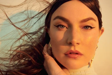 Close-up portrait of a woman with dark hair blowing in the wind, winged eyeliner, and golden hour lighting captured by Kate Powers.