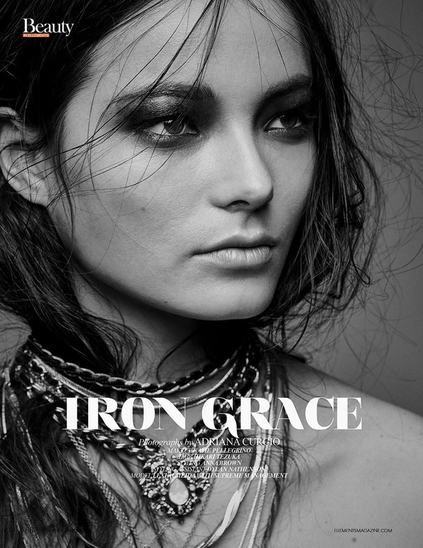 Black and white beauty shot of a woman with dark eye makeup wearing layered necklaces, looking off-camera in a studio setting.
