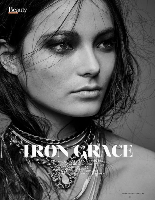 Black and white beauty shot of a woman with dark eye makeup wearing layered necklaces, looking off-camera in a studio setting.