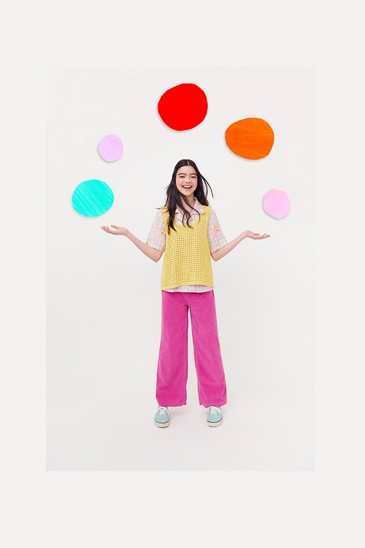 Young woman with long dark hair stands with arms out in a brightly lit white room, surrounded by colorful floating circles.