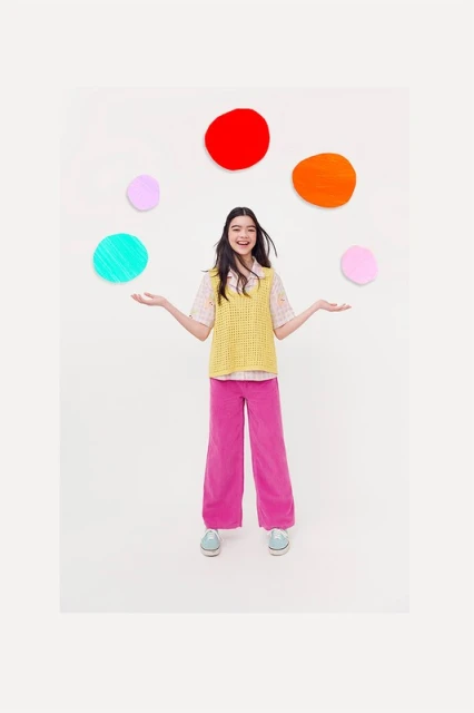 Young woman with long dark hair stands with arms out in a brightly lit white room, surrounded by colorful floating circles.
