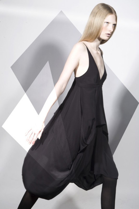 Fashionable young adult woman in black dress and leggings posing in a photo studio with geometric shapes in the background.