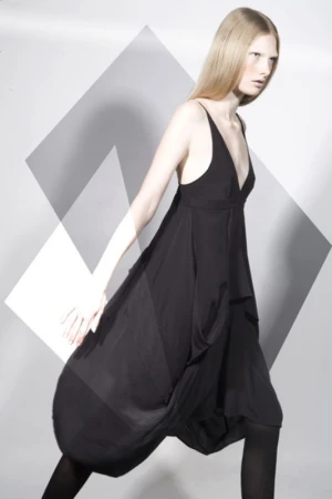Fashionable young adult woman in black dress and leggings posing in a photo studio with geometric shapes in the background.