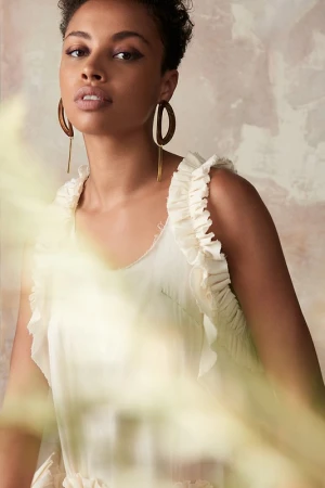 Portrait of a woman wearing a white ruffled top and large hoop earrings with makeup by Katie Pellegrino