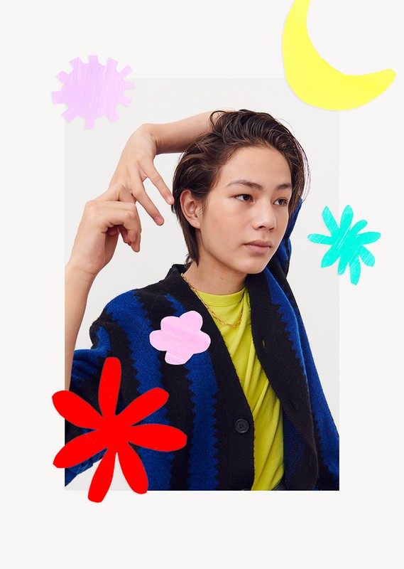 A young adult with short hair wearing a blue and black cardigan with colorful graphic overlays against a neutral backdrop.