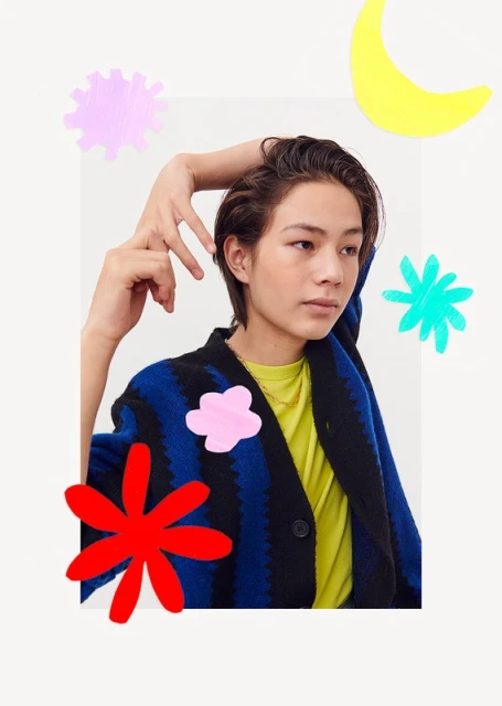 A young adult with short hair wearing a blue and black cardigan with colorful graphic overlays against a neutral backdrop.