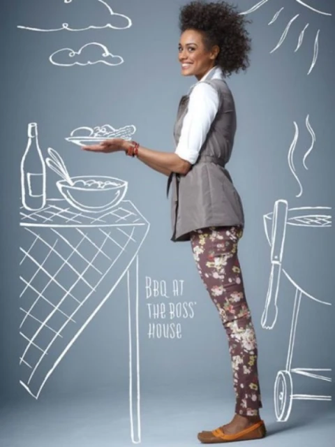Woman poses with salad on plate in studio, wearing patterned leggings, with a picnic table drawn in white on a grey background.