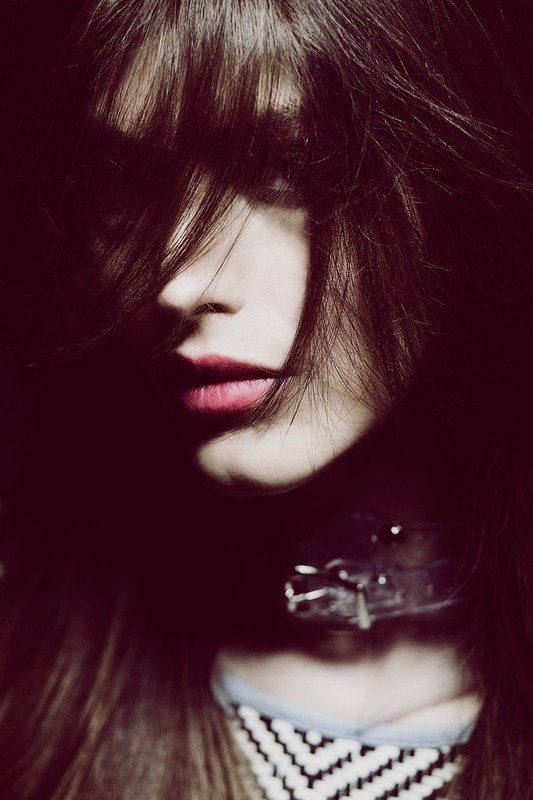 Close-up portrait of an adult woman with dark hair partially covering her face, wearing a collar necklace, and a black and white top.