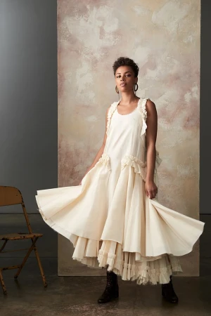 Model in cream ruffle dress holding skirt hem with makeup by Katie Pellegrino in studio