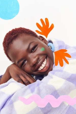 Close-up of a smiling African American woman wrapped in a lilac checkered blanket, adorned with colorful abstract paper art elements.