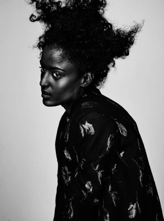 Black and white portrait of a woman with voluminous textured hair wearing a patterned jacket against a plain background