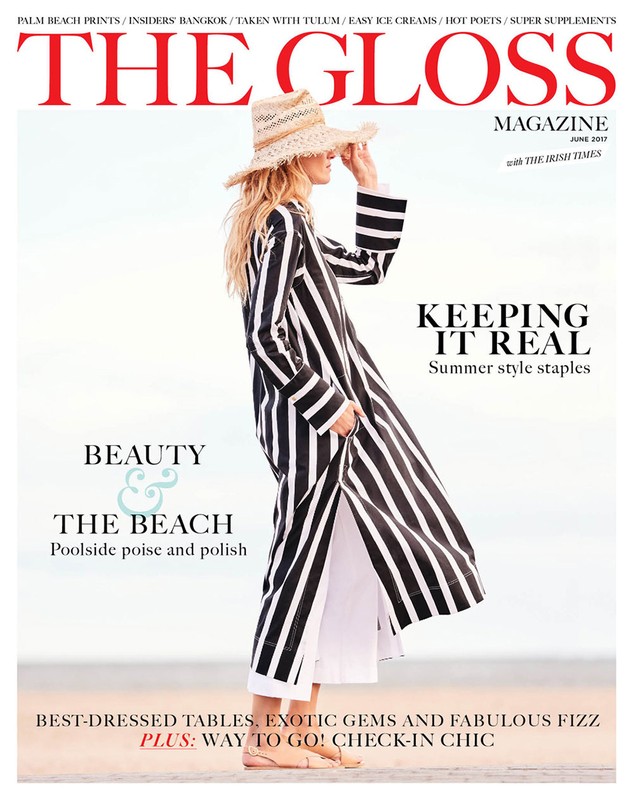 Fashion magazine cover featuring a woman in a striped robe and straw hat, standing on a beach with a light sky background.