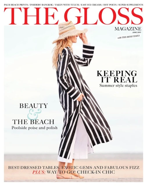 Fashion magazine cover featuring a woman in a striped robe and straw hat, standing on a beach with a light sky background.