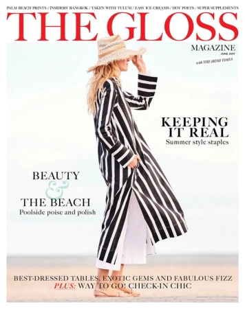 Fashion magazine cover featuring a woman in a striped robe and straw hat, standing on a beach with a light sky background.