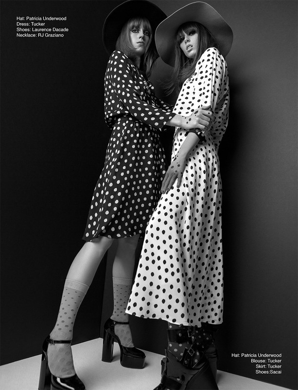 Two fashion models pose in polka dot dresses and hats against a dark background in a studio fashion shot. Monochrome styling.