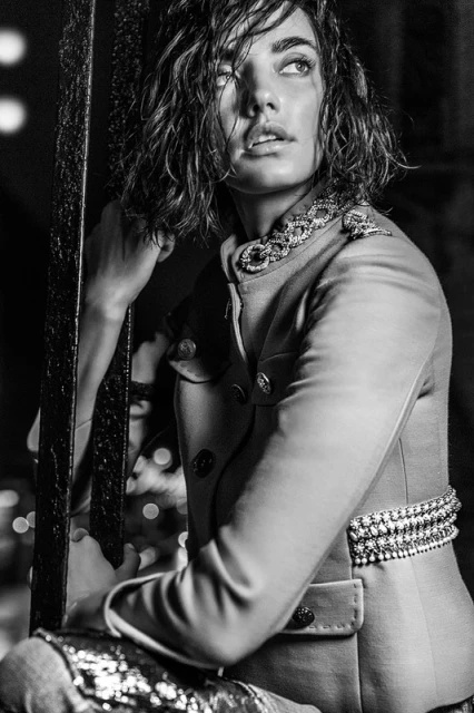 Monochrome portrait of a woman with wet hair in a military-style jacket, gazing upwards with soft lighting and shallow depth of field.